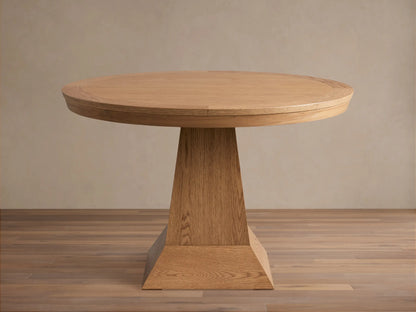 Leighton Round Dining Table in oak finish, featuring a smooth circular top and a wide, tapered pedestal base on a wood floor.