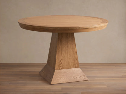 Leighton Round Dining Table in oak finish, featuring a smooth circular top and a wide, tapered pedestal base on a wood floor.