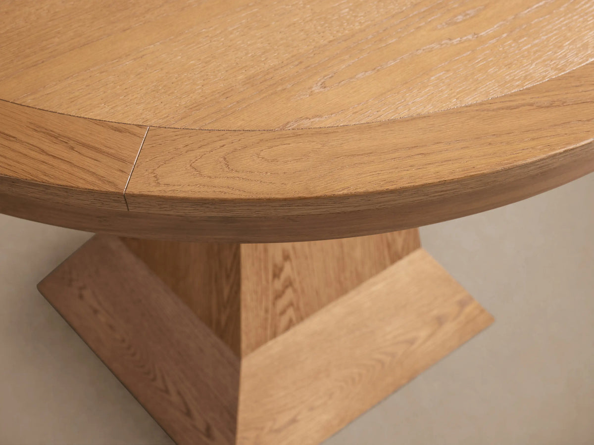 Leighton Round Dining Table in oak veneer on engineered hardwood, features a round top and a wide, angular pedestal base.