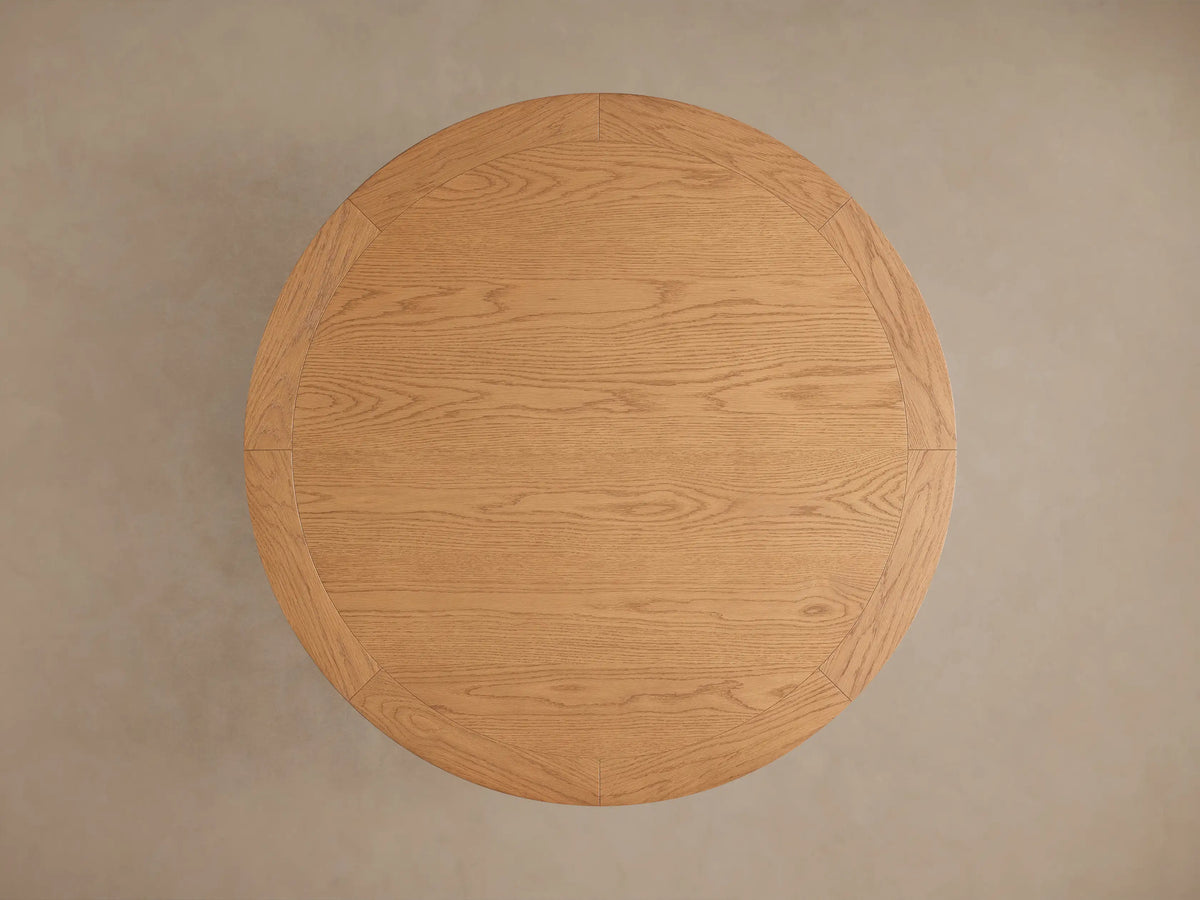 Leighton Round Dining Table with oak veneer top and pedestal base, showcasing warm wood tones and natural grain patterns.