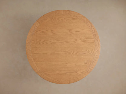 Leighton Round Dining Table with oak veneer top and pedestal base, showcasing warm wood tones and natural grain patterns.