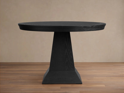 Leighton Round Dining Table in dark wood finish on a pedestal base. The table is placed on a wooden floor with a beige background.