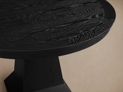 Leighton Round Dining Table in dark finish with a smooth, circular top and a sturdy, tapered pedestal base, displayed on wooden flooring.