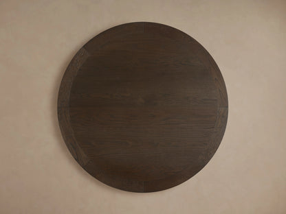 Round dining table with dark oak veneer and visible wood grain, featuring a thick edge and sturdy pedestal base on a neutral background.