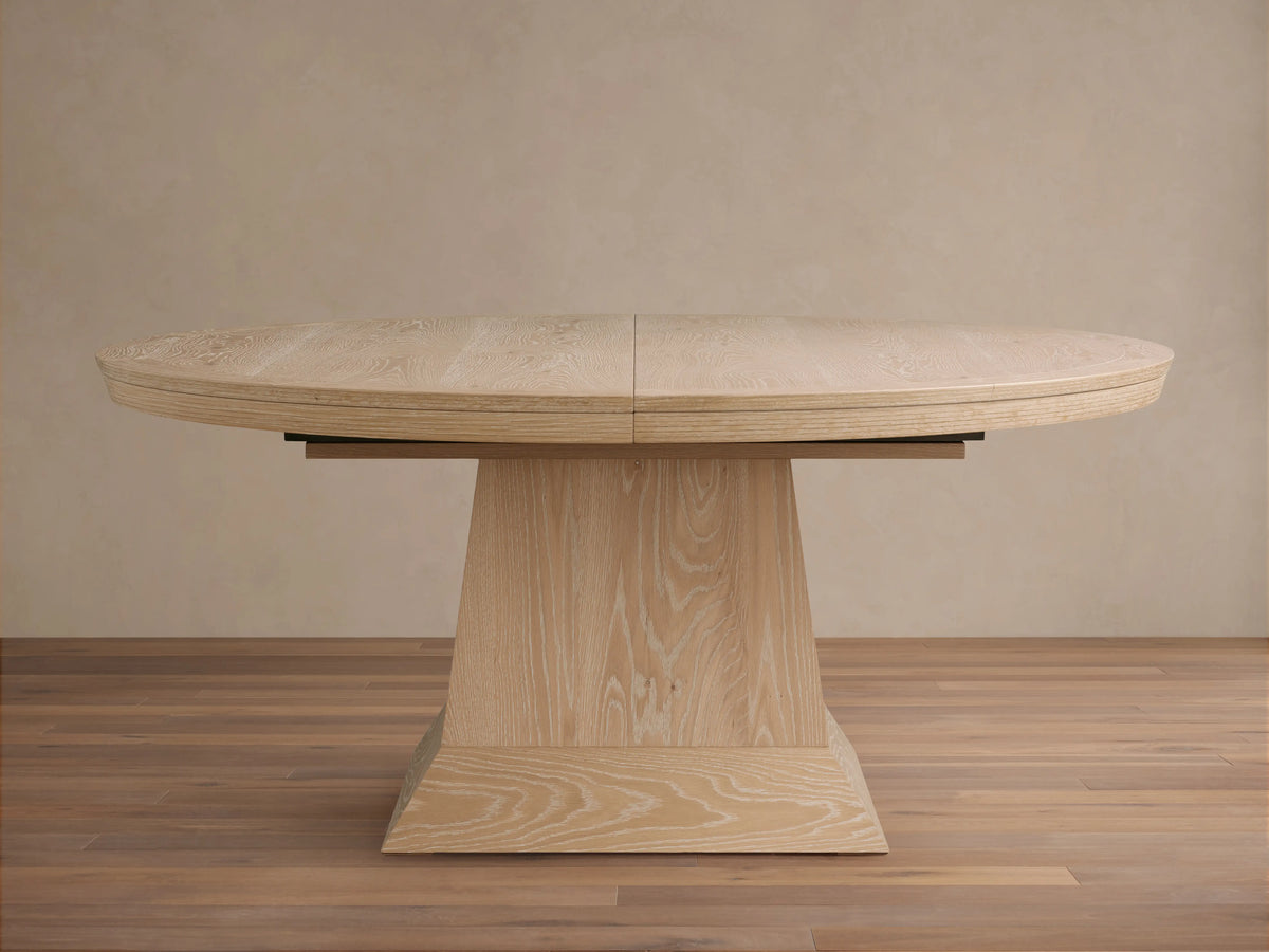 Leighton Extension Dining Table: oval, light blonde oak veneer top with visible grain and center seam, on a wide pedestal base.