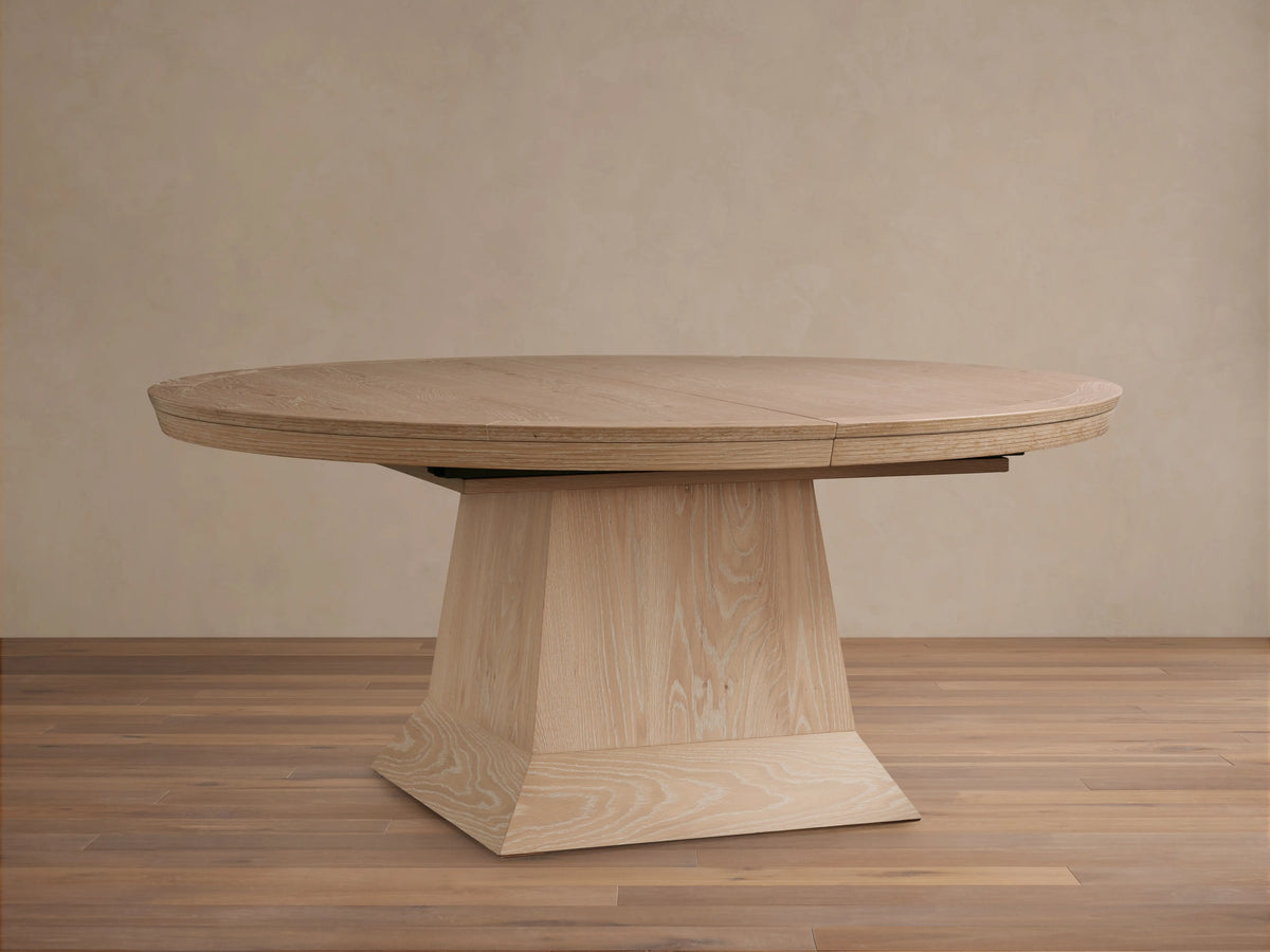 Light oak oval Leighton Extension Dining Table set with dinnerware in a stylish dining room with arch mirrors.
