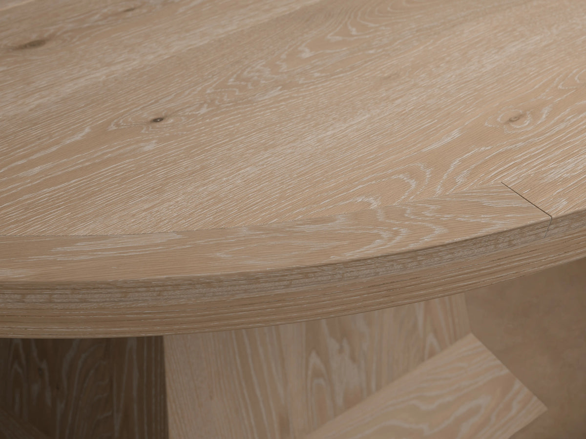 Leighton Extension Dining Table, light oak with round top & visible seam for extension, sturdy geometric pedestal base, on wood floor.