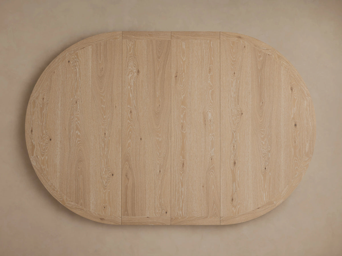 Overhead, round Leighton Extension Dining Table with light oak veneer top showing natural wood grain, on a pale beige background.