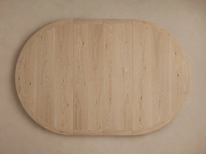 Overhead, round Leighton Extension Dining Table with light oak veneer top showing natural wood grain, on a pale beige background.