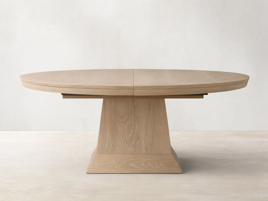 Leighton Extension Dining Table: oval, light blonde oak veneer top with visible grain and center seam, on a wide pedestal base.