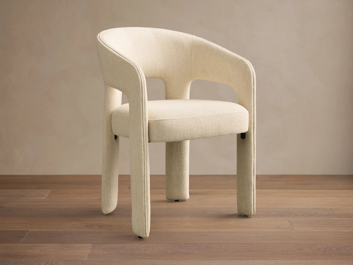 Front view of a cream Lilette Dining Arm Chair, fully upholstered, with a rounded back and thick integrated arms.