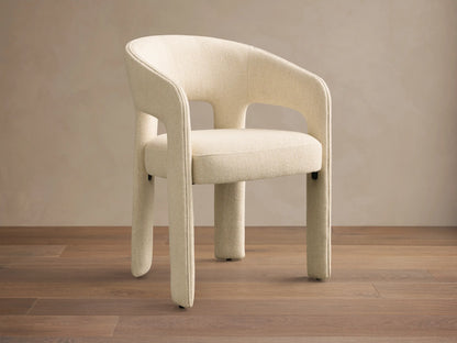 Front view of a cream Lilette Dining Arm Chair, fully upholstered, with a rounded back and thick integrated arms.