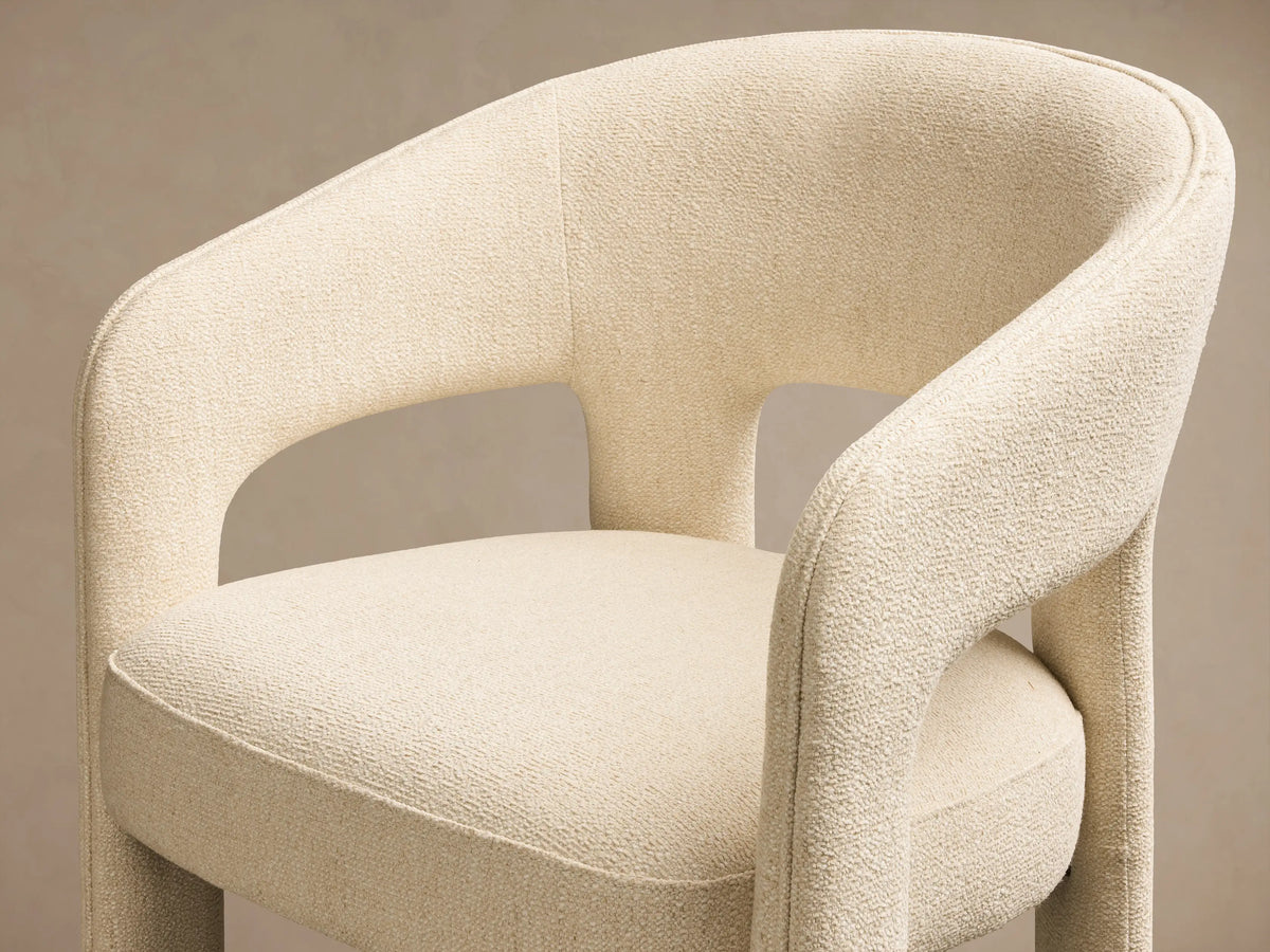 Front view of a cream Lilette Dining Arm Chair, fully upholstered, with a rounded back and thick integrated arms.