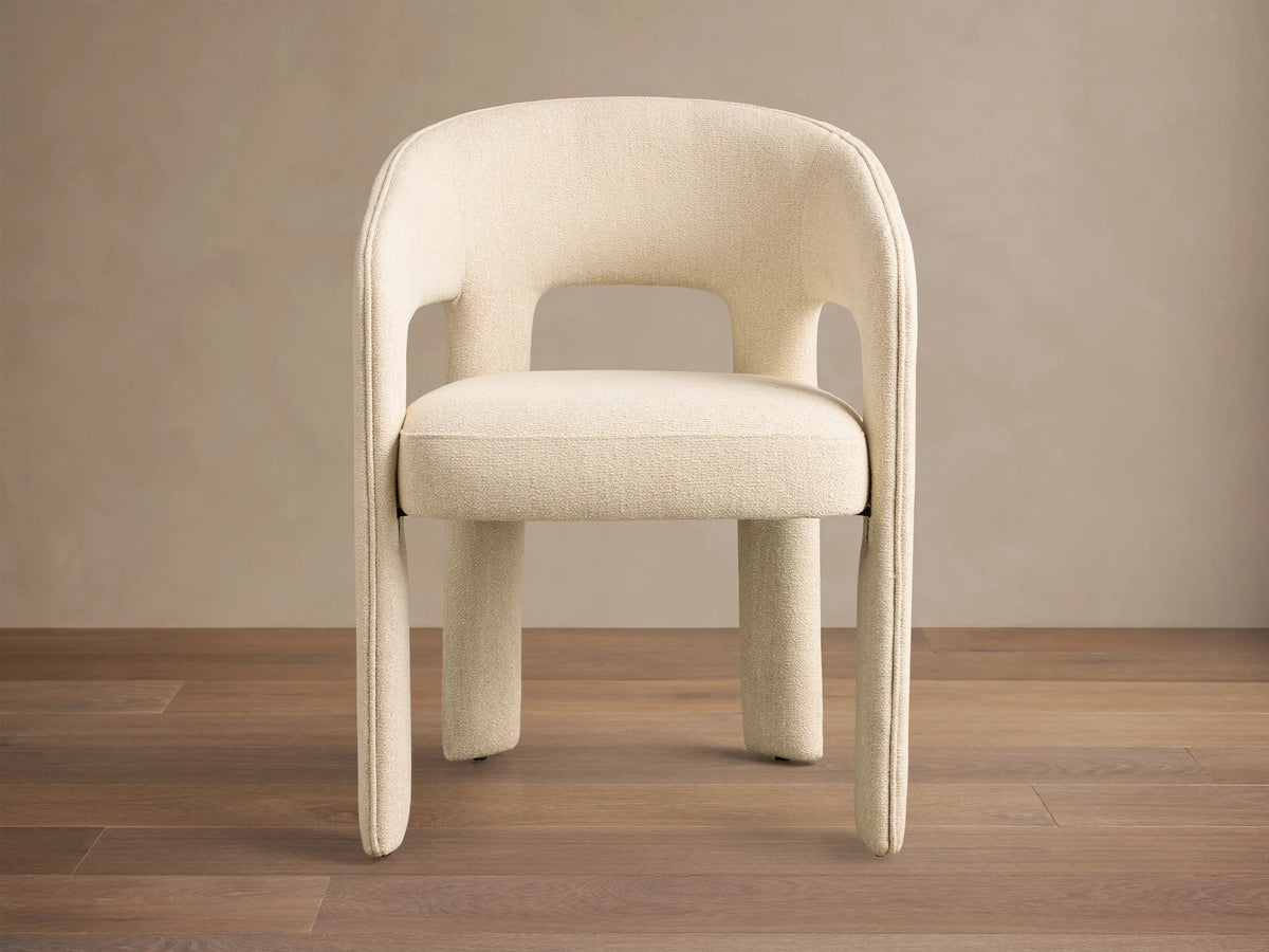 Close-up of the cream textured Lilette Dining Arm Chair, showing its curved back and armrests.