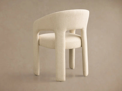 Side profile of a cream Lilette Dining Arm Chair, fully upholstered in textured fabric with a curved back, armrests, and thick legs.