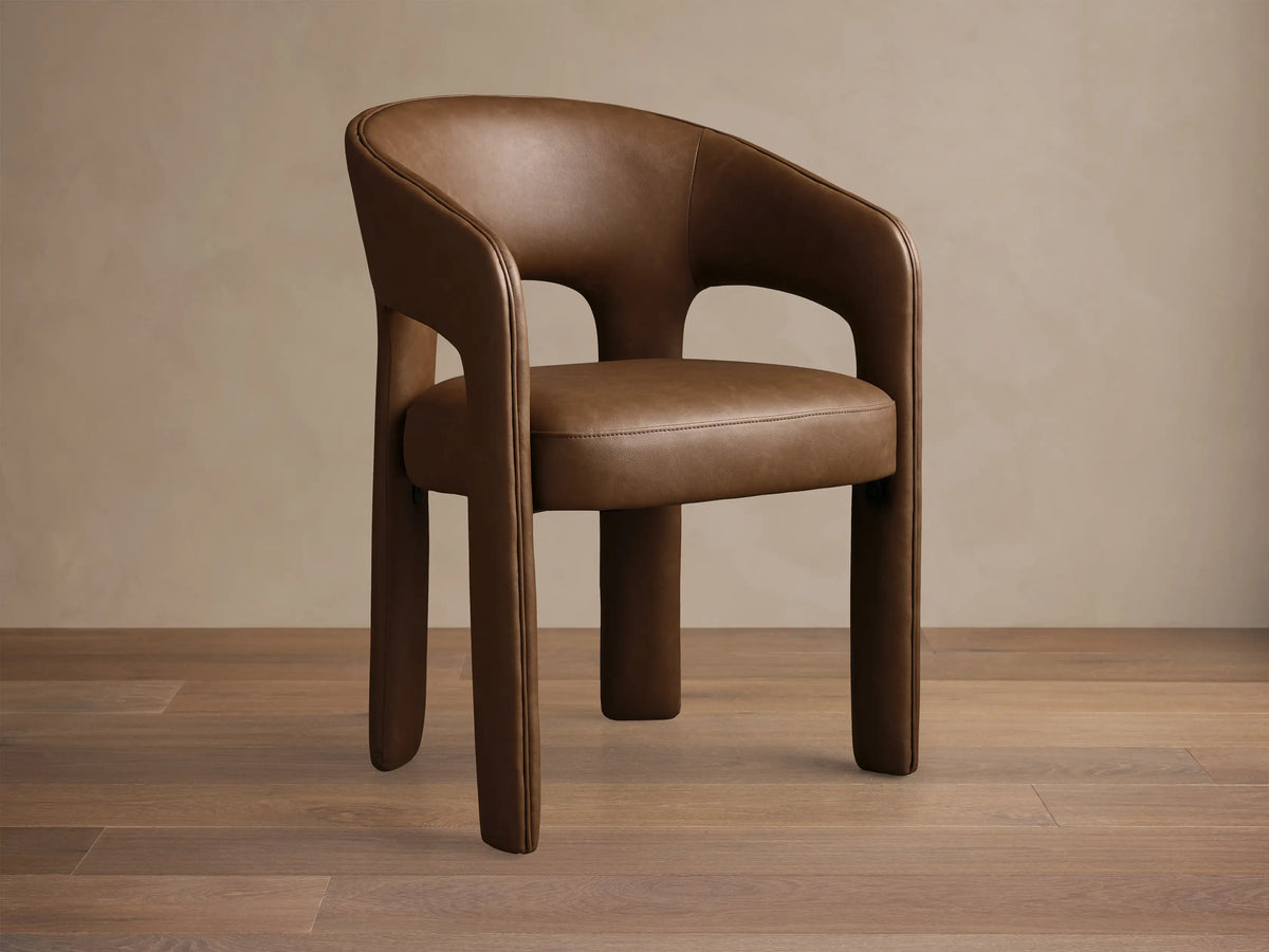 Front view of the brown Lilette Faux Leather Dining Arm Chair, featuring a curved back and integrated armrests.