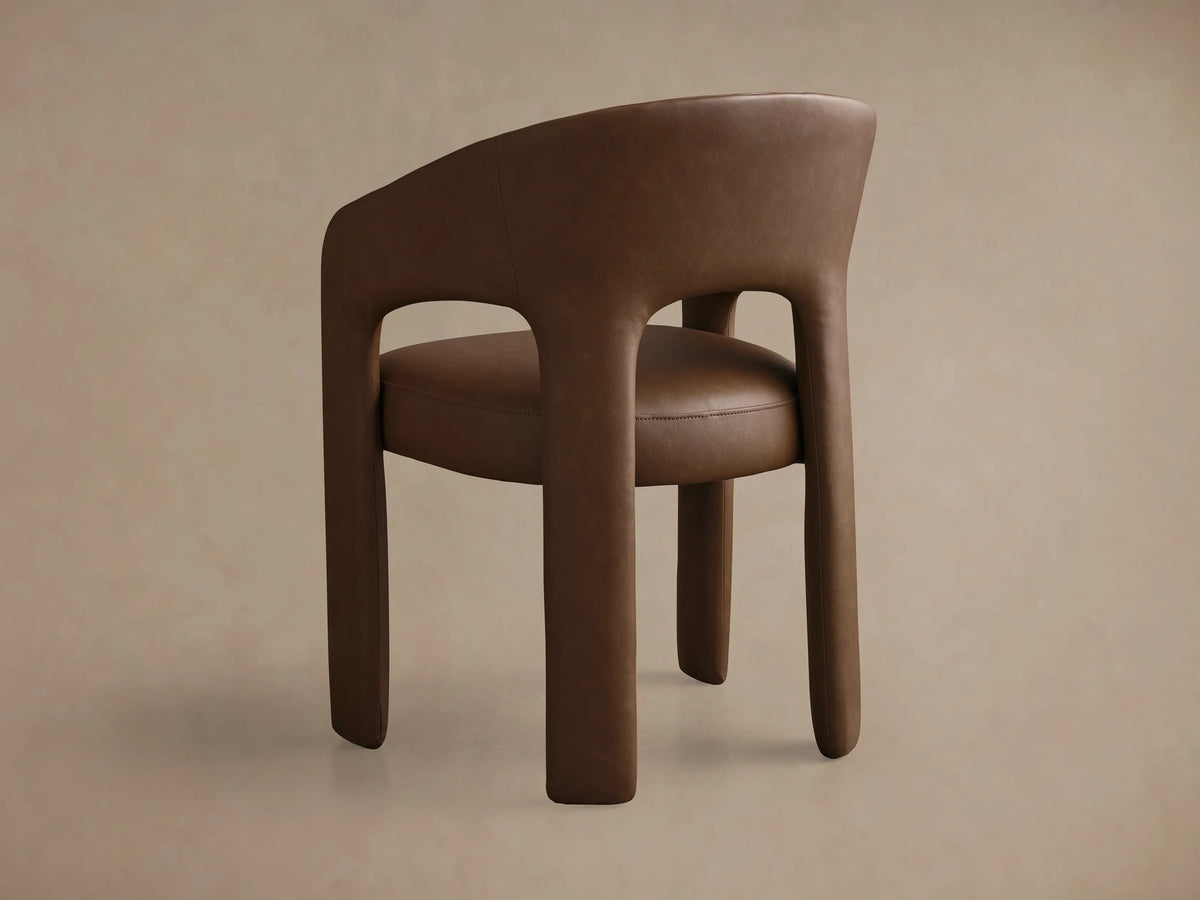 Front view of the brown Lilette Faux Leather Dining Arm Chair, featuring a curved back and integrated armrests.