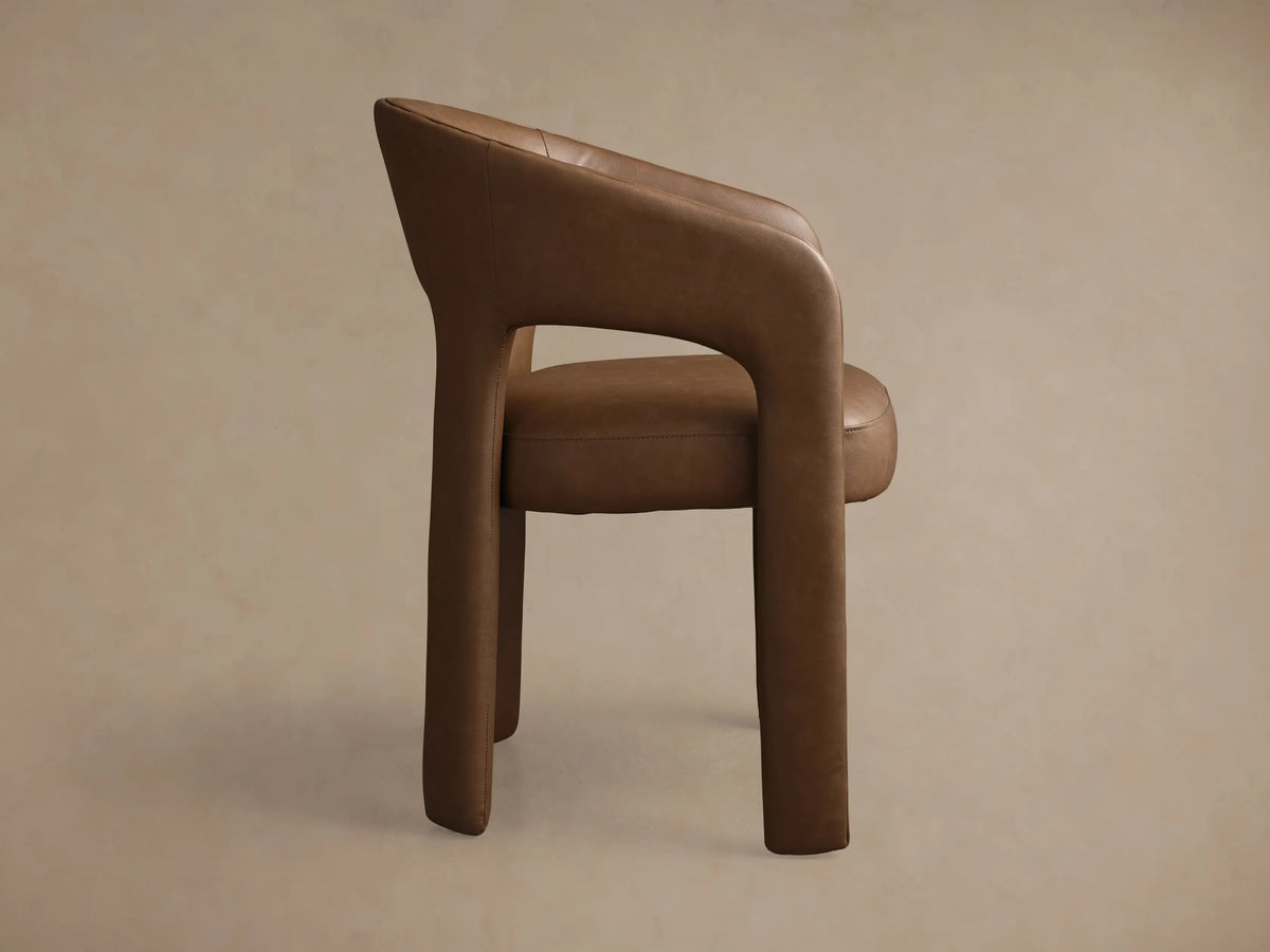 Close-up of the rich brown Lilette Faux Leather Dining Arm Chair, highlighting its curved back, integrated armrests, and faux leather texture.