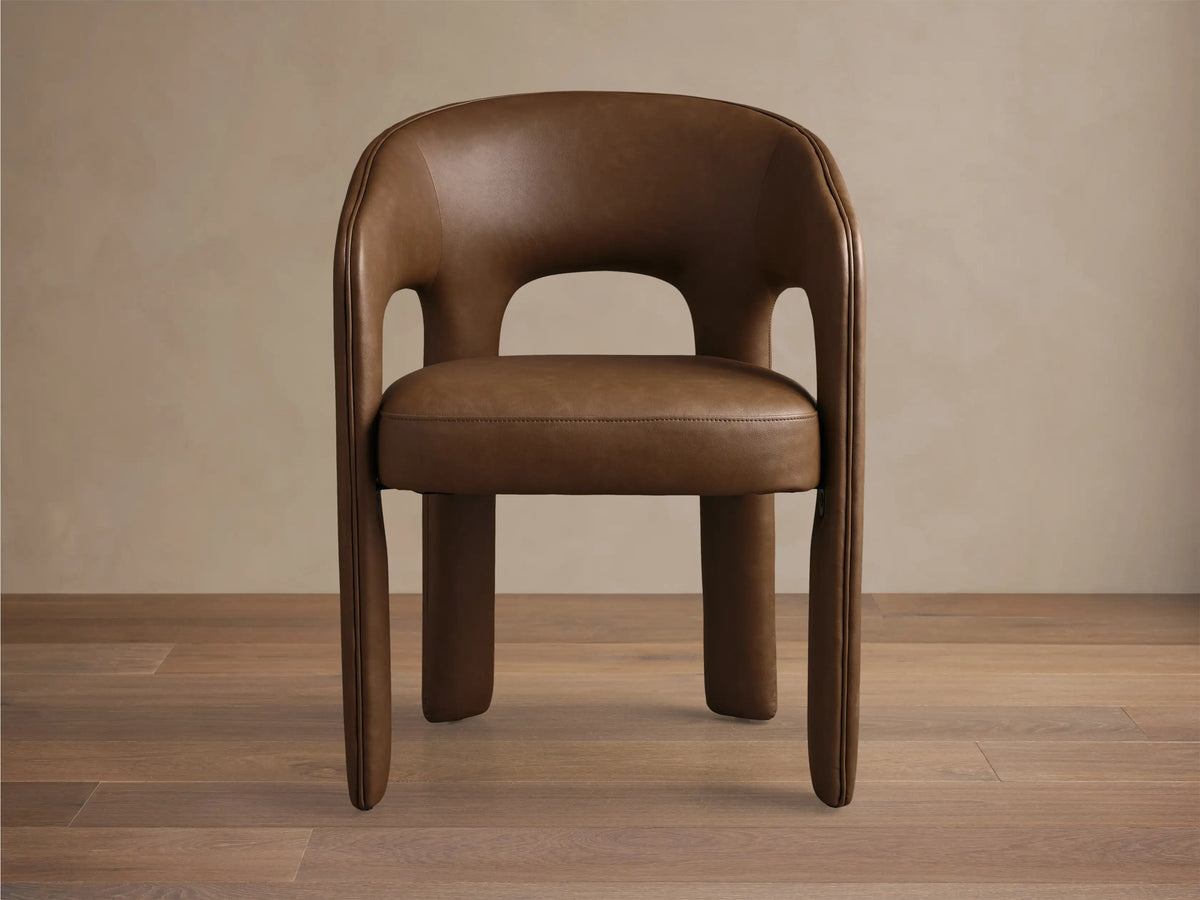 Side profile of the brown Lilette Faux Leather Dining Arm Chair, showing its curved back and integrated armrests.