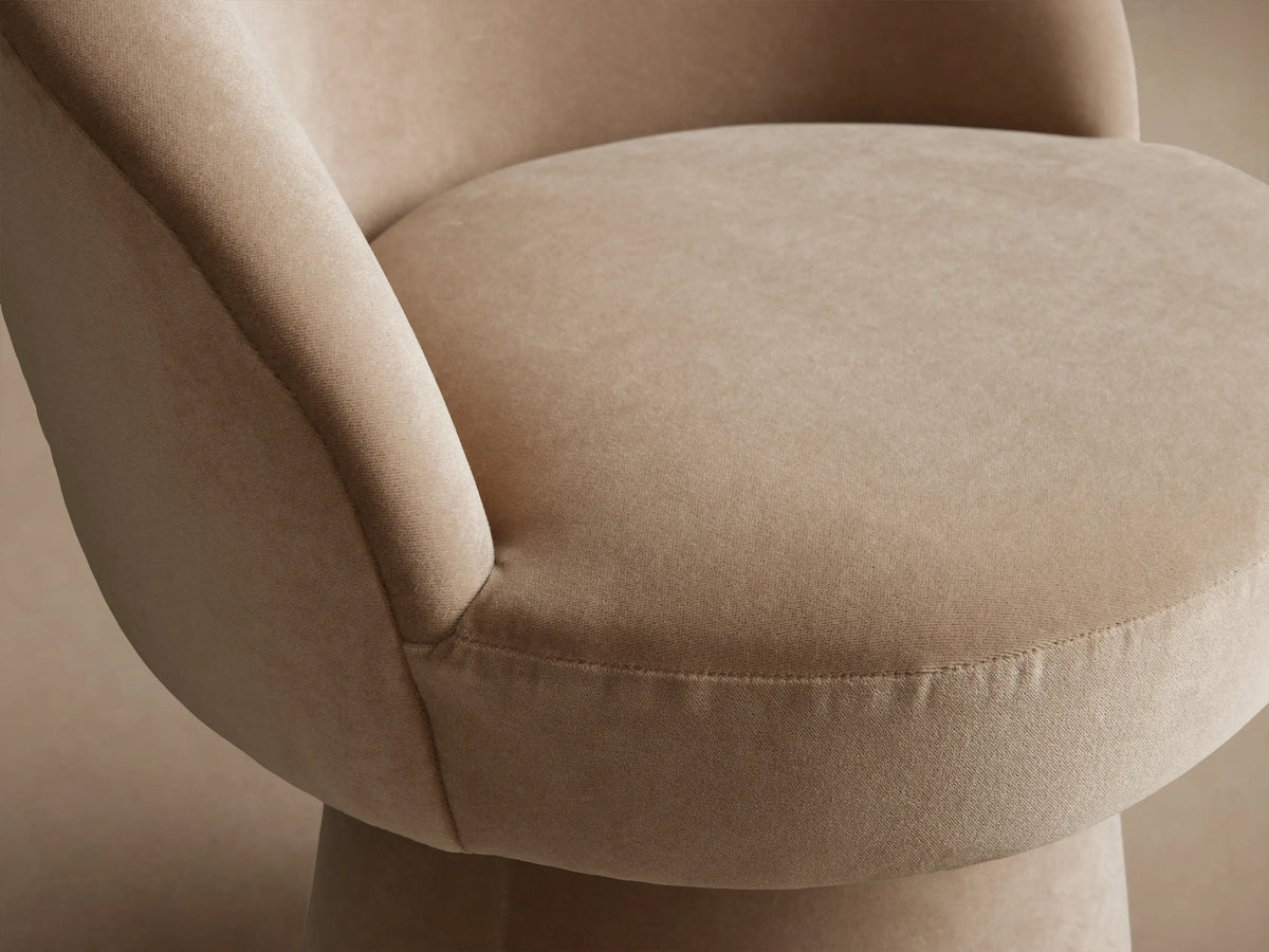 Lindsay Swivel Dining Chair in light beige fabric, features a rounded back and cylindrical base on a wooden floor.