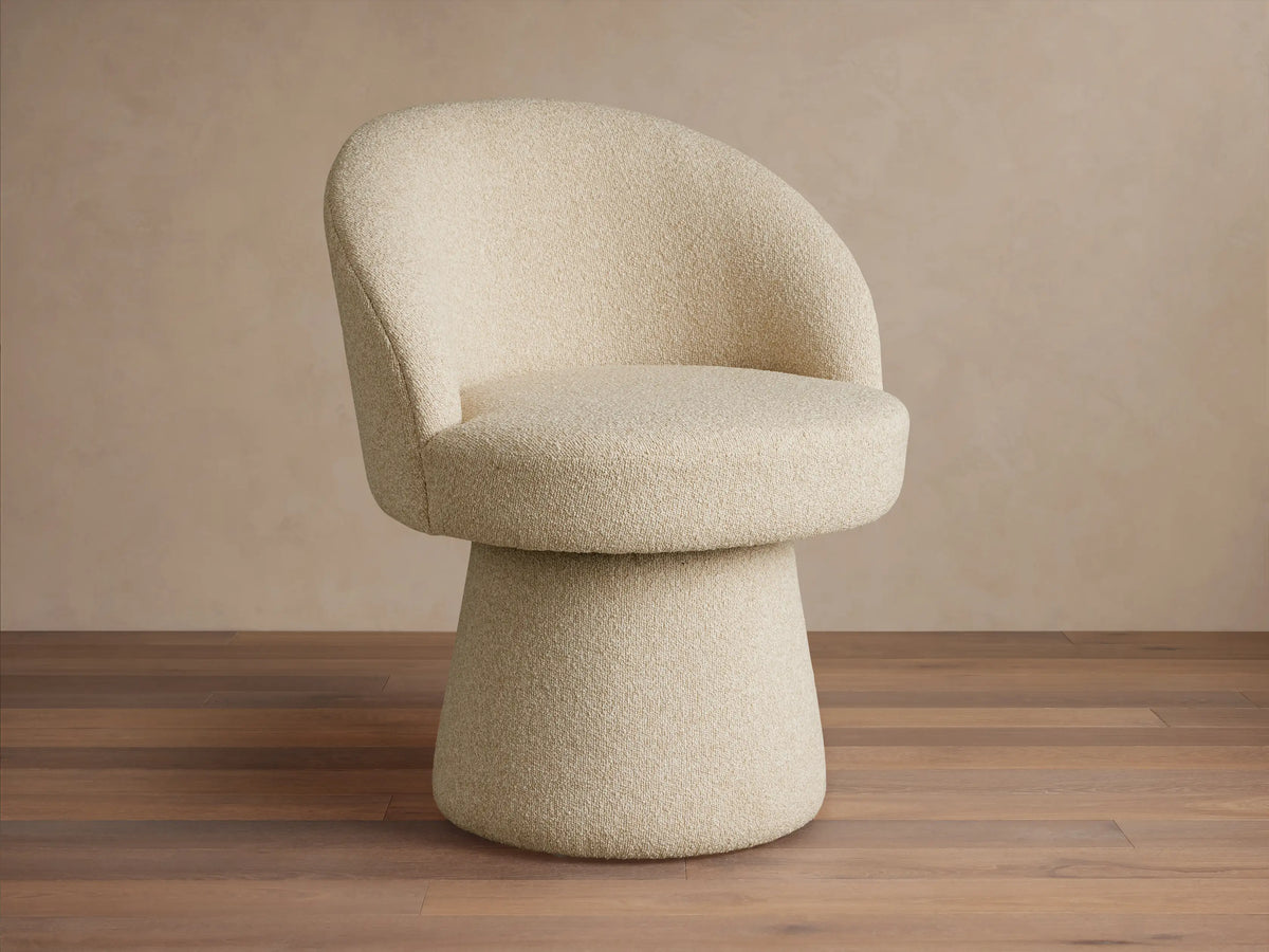 Lindsay Swivel Dining Chair in beige fabric, featuring a curved backrest and round cushioned seat on a tapered base, on a wooden floor.