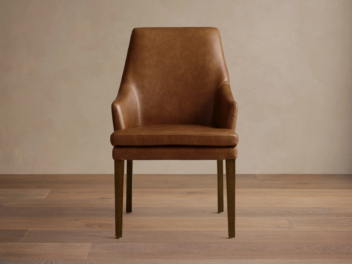 Lunden Faux Leather Dining Arm Chair in brown, featuring a gently curved backrest and armrests, on wooden legs.