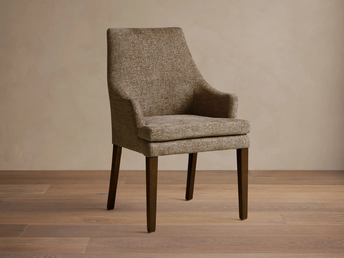Lunden Dining Arm Chair in textured brown fabric, featuring a gently curved backrest and wooden legs on a wooden floor.