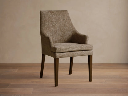 Lunden Dining Arm Chair in textured brown fabric, featuring a gently curved backrest and wooden legs on a wooden floor.
