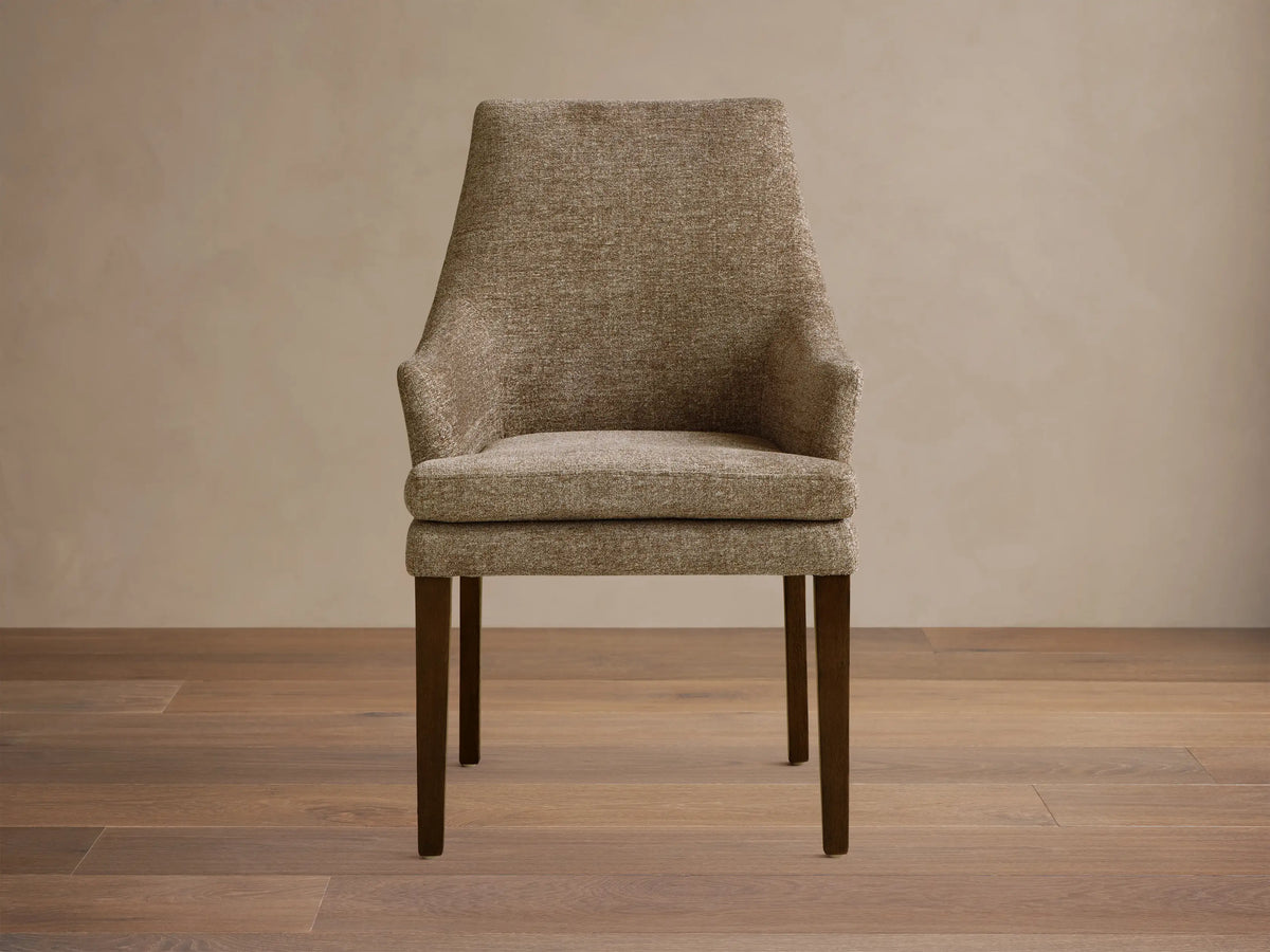 Lunden Dining Arm Chair in textured brown fabric, featuring a gently curved backrest and wooden legs on a wooden floor.