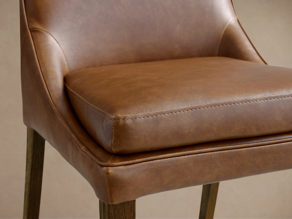 Lunden Dining Side Chair with a hand-stained brown leather seat, gently curved backrest, and dark wooden legs on wooden floor.