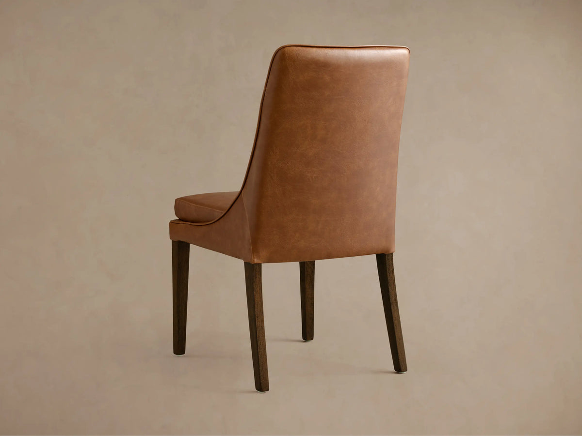 Lunden Dining Side Chair with brown leather seat and curved backrest on wooden legs. Hand-stained finish adds sheen.