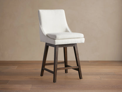 Lunden Swivel Stool with curved off-white upholstered seat and back, on a dark wood frame, angled right on a wood floor.