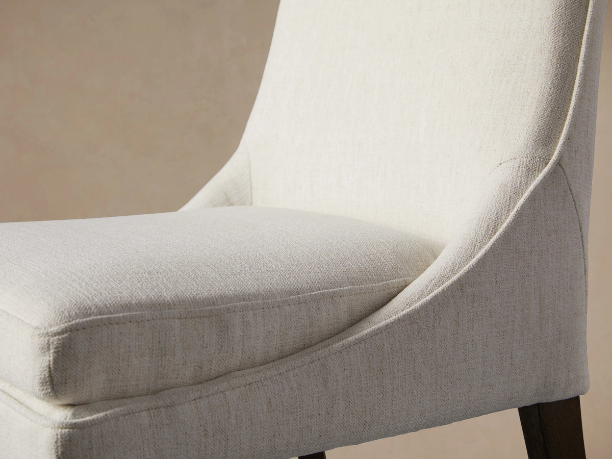 Lunden Swivel Stool, front view. Off-white upholstered seat & curved back on dark wood legs. Set against tan wall, hardwood floor.