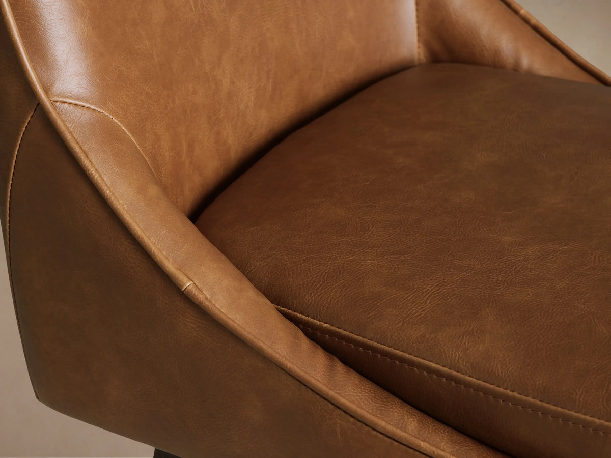 Lunden Faux Leather Swivel Stool with caramel-colored upholstered seat and backrest, wooden base, and footrests on a hardwood floor.