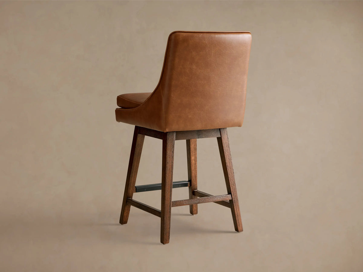 Lunden Faux Leather Swivel Stool close-up showing brown faux leather upholstery, curved backrest, and cushioned seat.