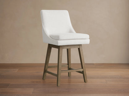 Lunden Swivel Stool in Fawn with soft cream fabric, gently curved backrest, and wooden legs on hardwood floor.