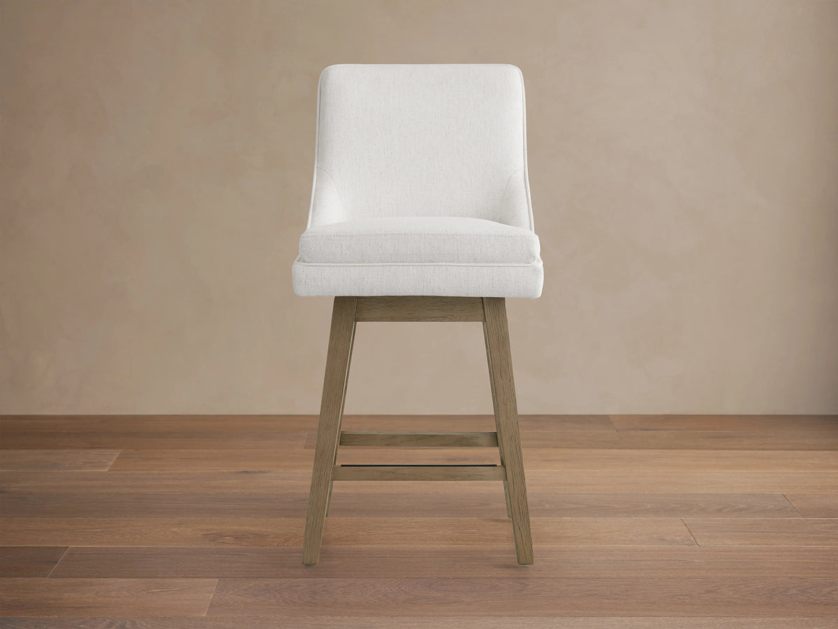 Lunden Swivel Stool in Fawn with soft cream fabric, gently curved backrest, and wooden legs on hardwood floor.