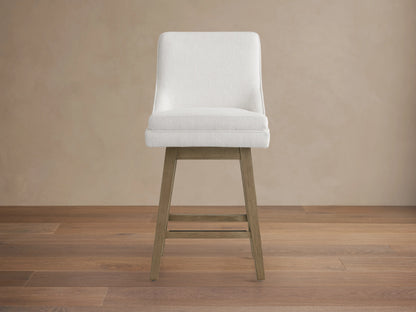 Lunden Swivel Stool in Fawn with soft cream fabric, gently curved backrest, and wooden legs on hardwood floor.