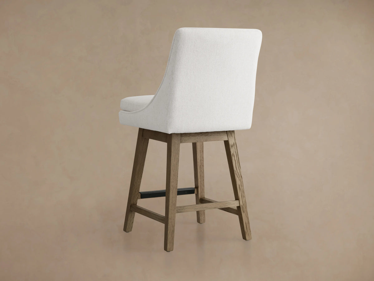 Lunden Swivel Stool in Fawn with a cushioned seat in light beige fabric and a gently curved backrest on a wooden base.