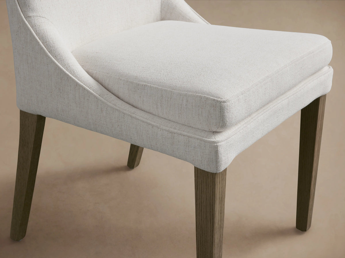 Lunden Dining Side Chair in Fawn shown from the front, features a softly curved backrest, cushioned seat, and wooden legs on a wooden floor.