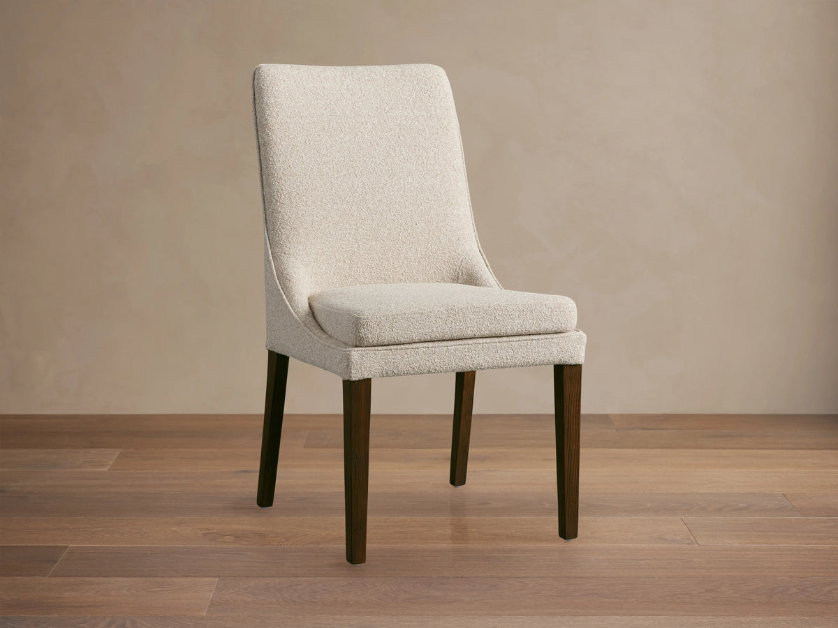 Lunden Dining Side Chair with a beige upholstered seat and backrest, featuring curved design and dark wooden legs on a wooden floor.
