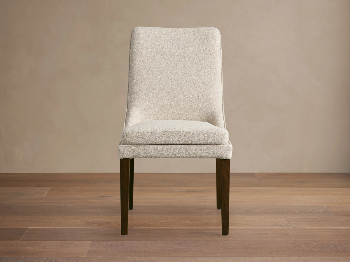 Lunden Dining Side Chair with a beige upholstered seat and backrest, featuring curved design and dark wooden legs on a wooden floor.