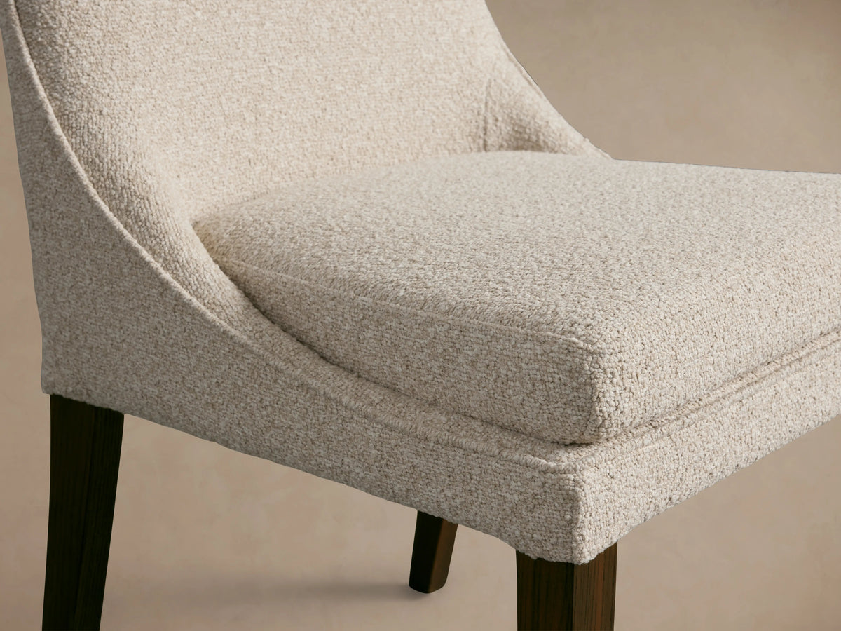 Lunden Dining Side Chair with cream fabric, gently curved backrest, cushioned seat, dark wooden legs, on a wooden floor.