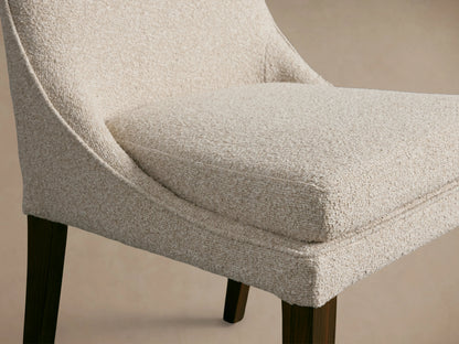 Lunden Dining Side Chair with cream fabric, gently curved backrest, cushioned seat, dark wooden legs, on a wooden floor.