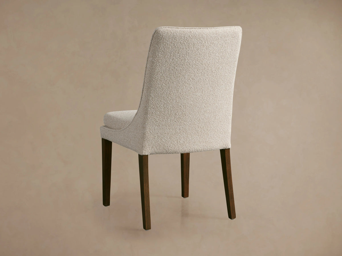 Lunden Dining Side Chair with curved backrest, upholstered in light beige fabric. Dark wooden legs visible, shown in side view.