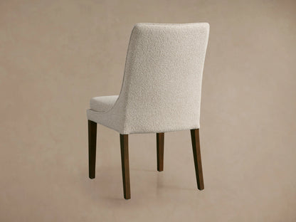 Lunden Dining Side Chair with curved backrest, upholstered in light beige fabric. Dark wooden legs visible, shown in side view.