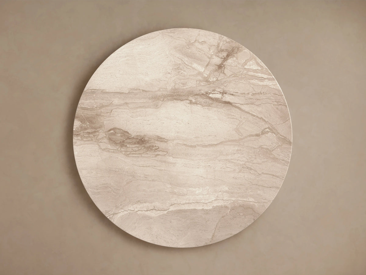 Modena Dining Table with round Italian Beige Coralle marble top & faceted pedestal base, front view, against a beige wall & wooden floor.