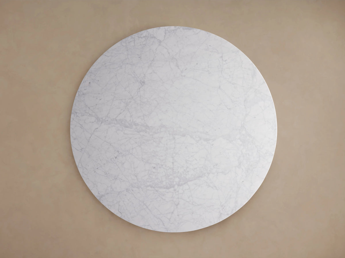 Modena Dining Table. Close-up of smooth white marble top with grey veining. Part of marble base visible against beige wall.