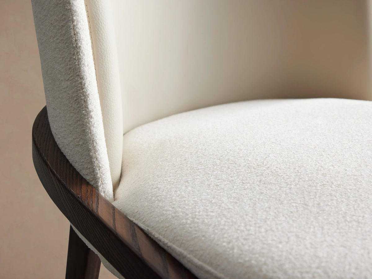Mena Dining Chair close-up showing beige seat cushion and smooth backrest, with dark wood frame visible on the side.