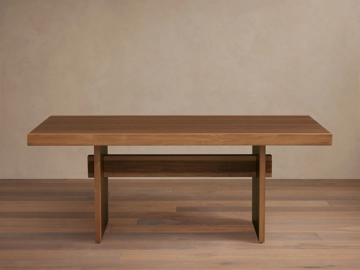 Mihaela Dining Table made from Romanian oak and spruce with walnut veneer. Features a sleek rectangular top and unique cross-beam legs on wooden floor.